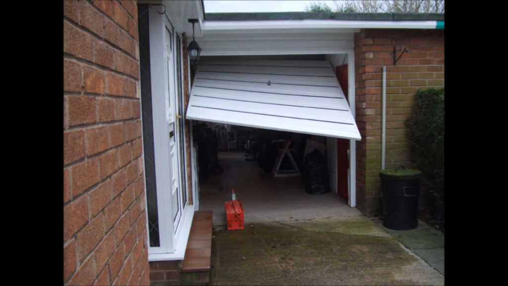 Up-and-over garage door stuck partly open and tilted on its frame, needing repair