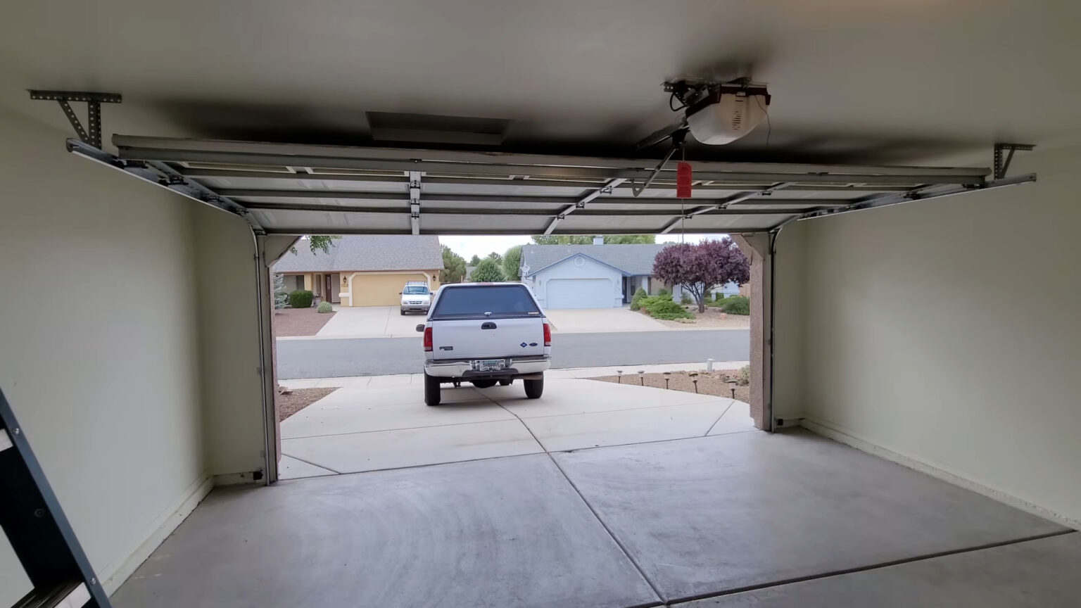 Open garage door seen from inside, showing the opener rail, horizontal tracks and red emergency release cord