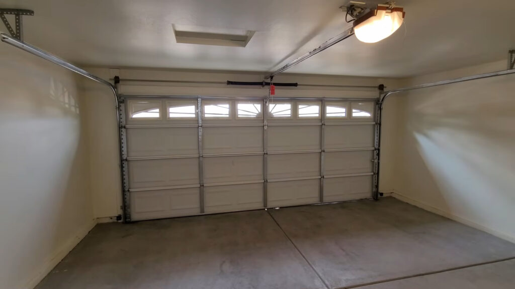 Closed two-car garage door seen from inside, with the torsion spring on the bar above the door and a ceiling-mounted opener